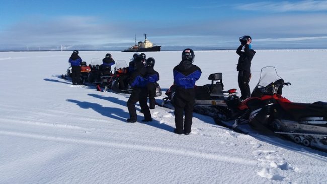 Excursión con moto de nieve en el mar Báltico. Al fondo el rompehielos Sampo 